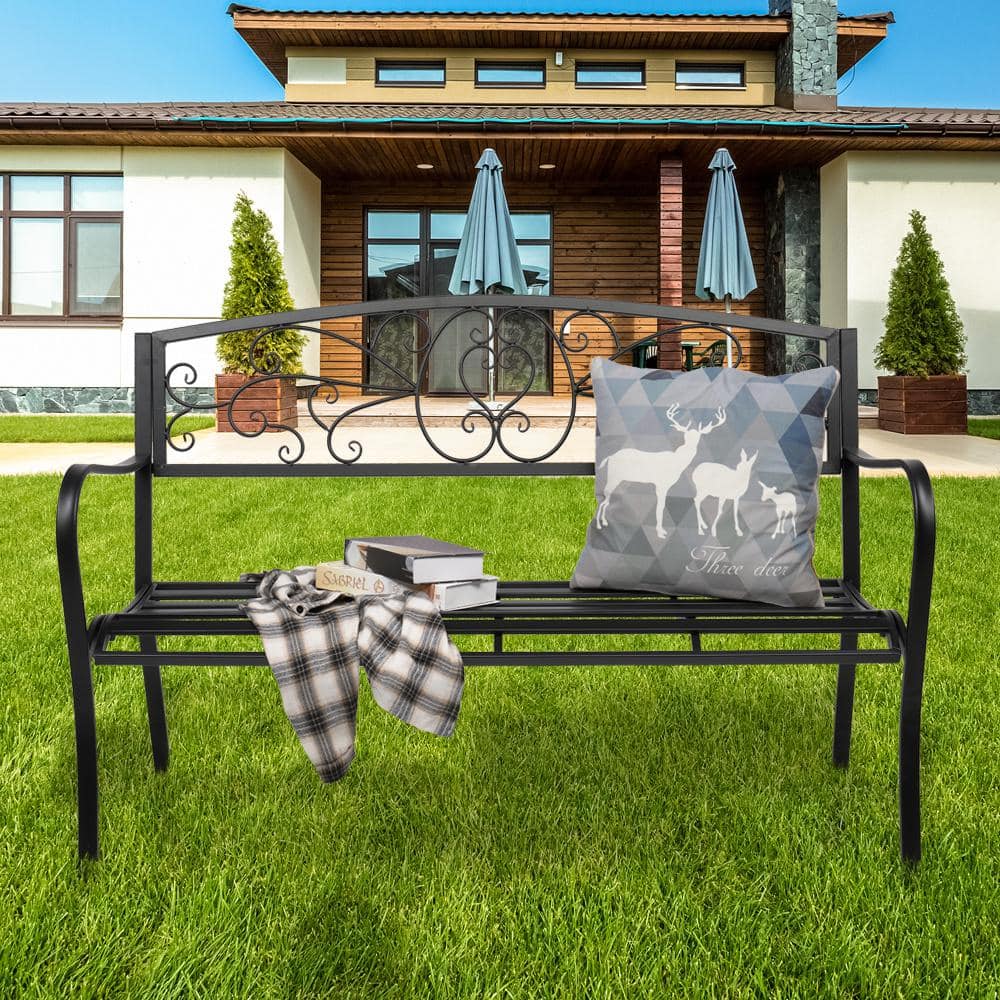 Black metal outdoor bench on a green lawn in front of a house.