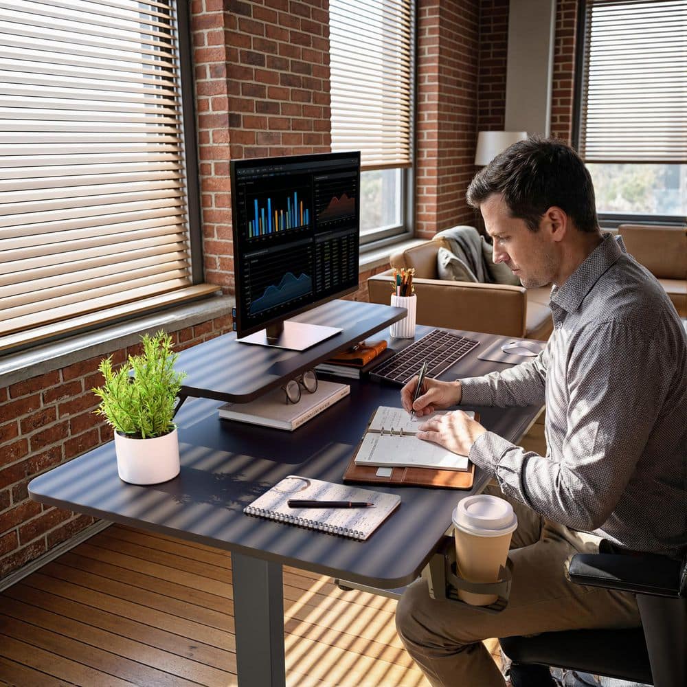 Person using a black electric standing desk in a bright room.