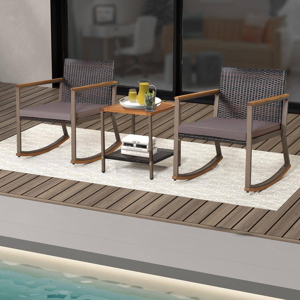 Two wicker rocking chairs with grey cushions and a two-tier acacia wood side table on a light rug.