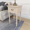 Cream end table with a lamp on top next to a sofa.