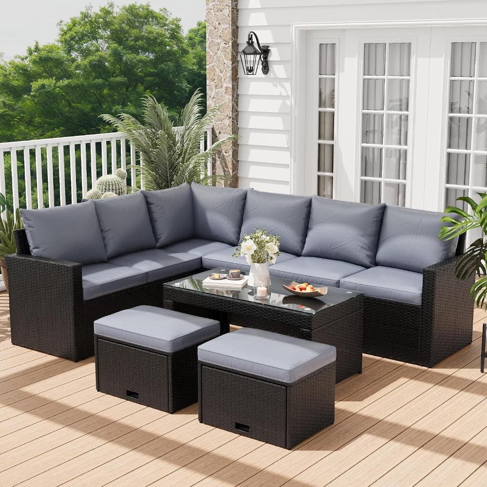 Wicker outdoor sectional sofa set with gray cushions and two ottomans on a wooden deck.