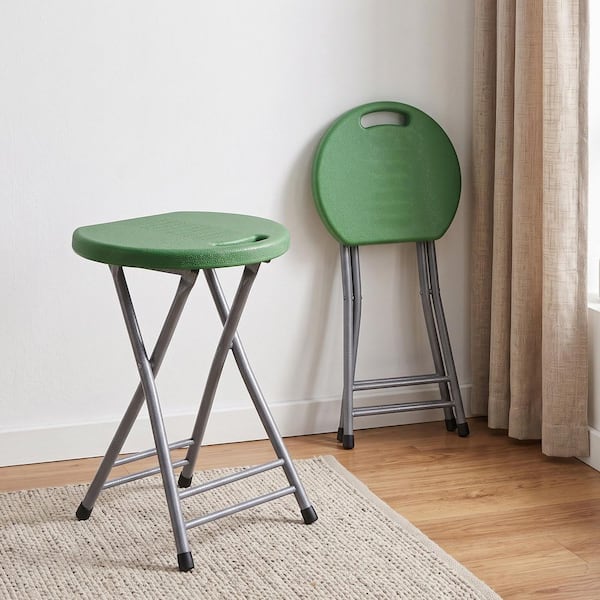 Green folding stool with metal X-frame base on a rug.