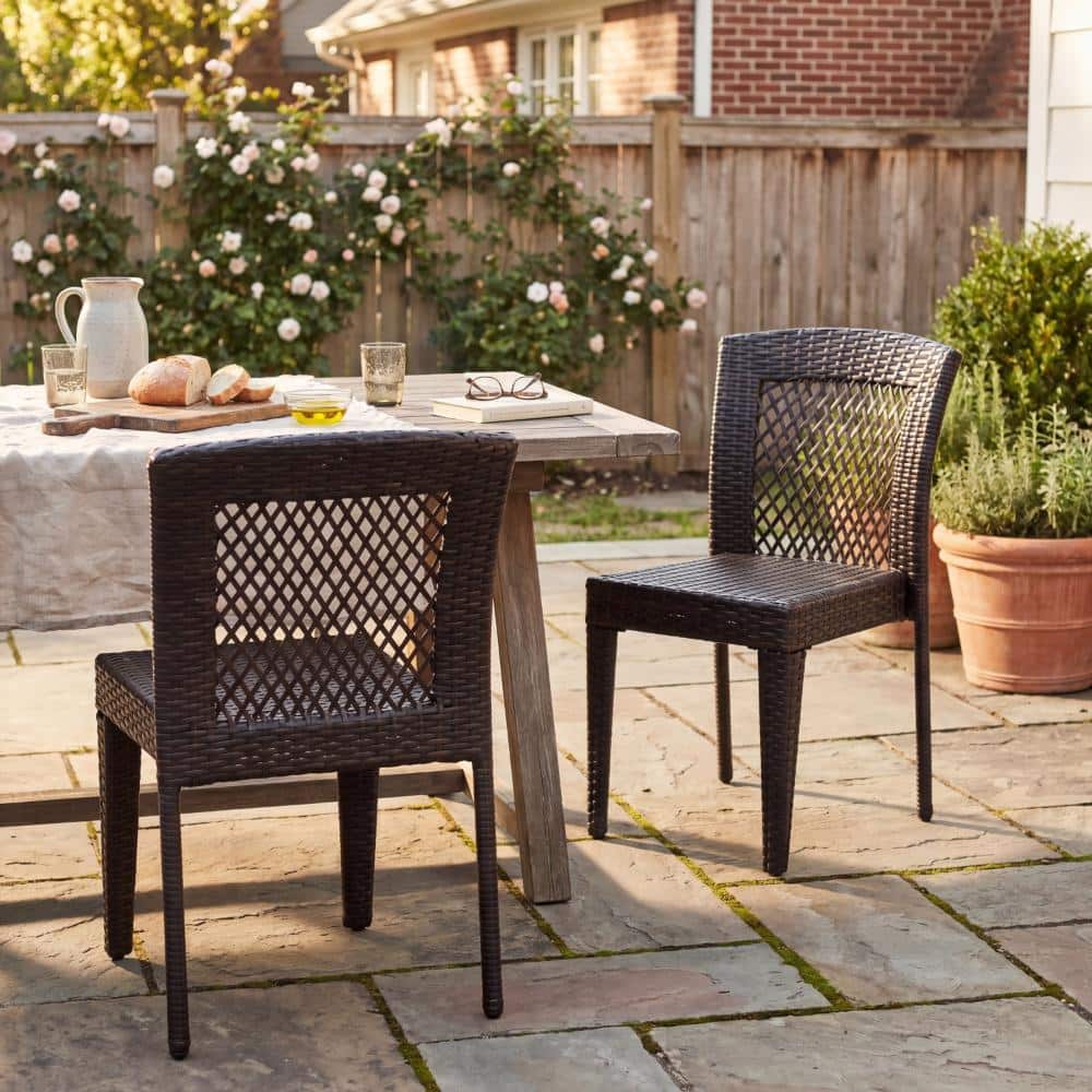 Two black woven outdoor dining chairs on a stone patio next to a table.