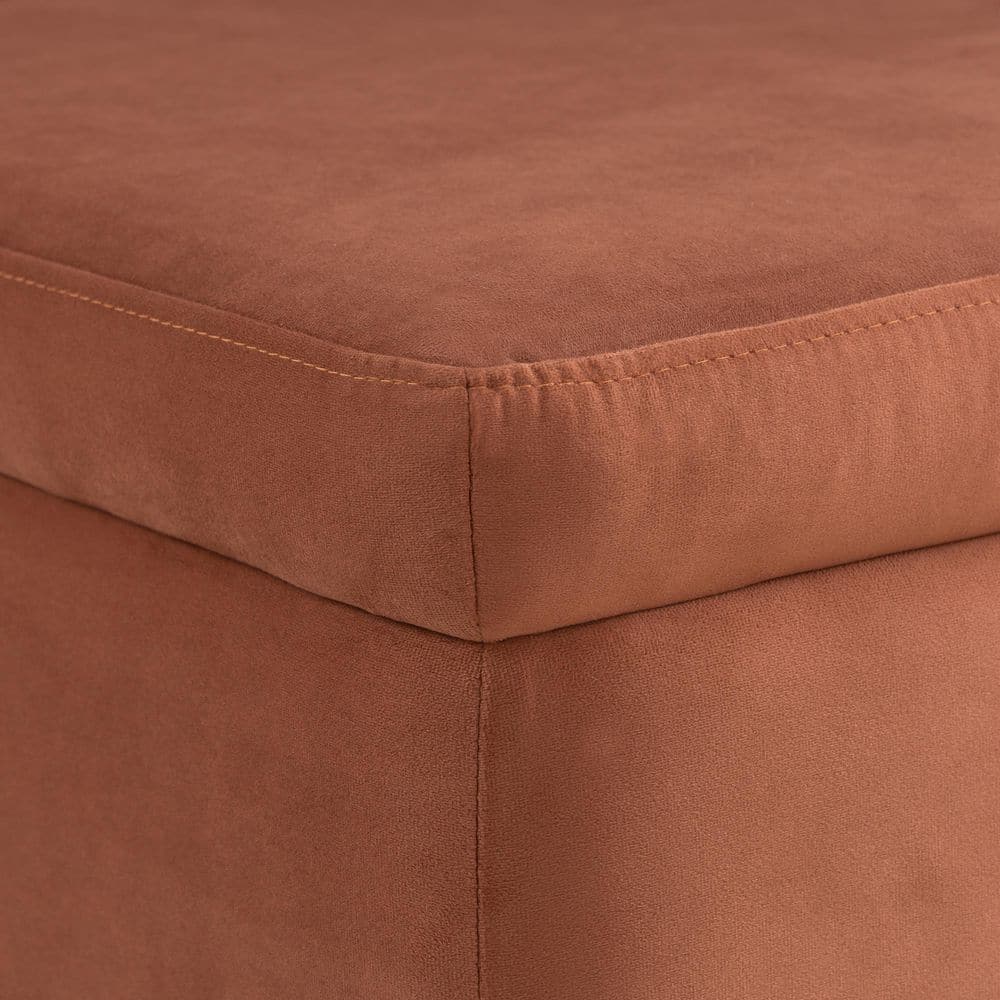 Close-up of the corner of a rust velvet storage ottoman.
