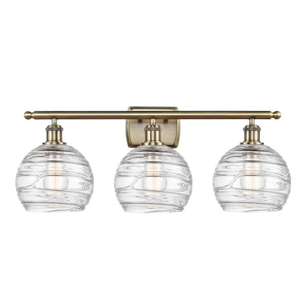Athens Deco Swirl 26 in. 3-Light Clear Deco Swirl, Antique Brass Vanity Light with Clear Glass Shade