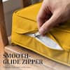 Hand pulling the smooth-glide zipper on a yellow cushion cover.