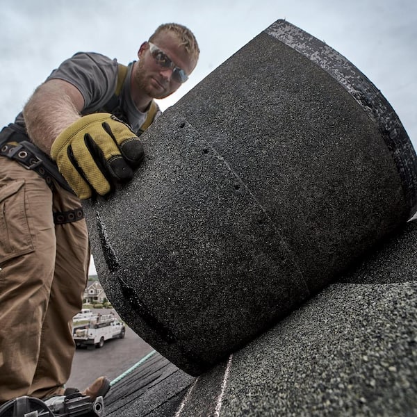 Roof repair, worker with white gloves replacing gray tiles or shingles on  house with blue sky