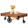 Brown rustic industrial coffee table with black cast iron wheels on a white background.