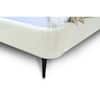 Close-up of the corner and black tapered leg of a white velvet upholstered bed.