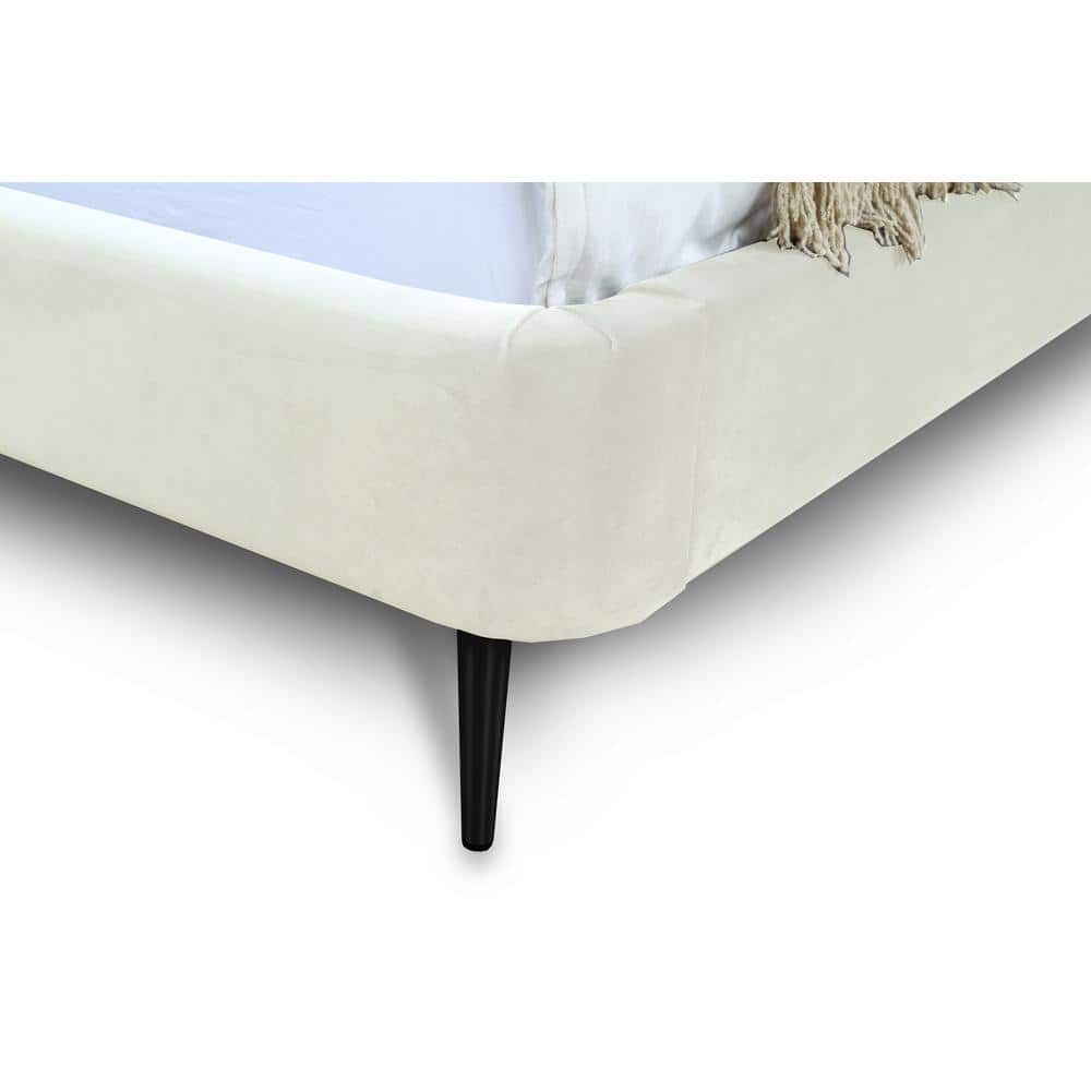 Close-up of the corner and black tapered leg of a white velvet upholstered bed.
