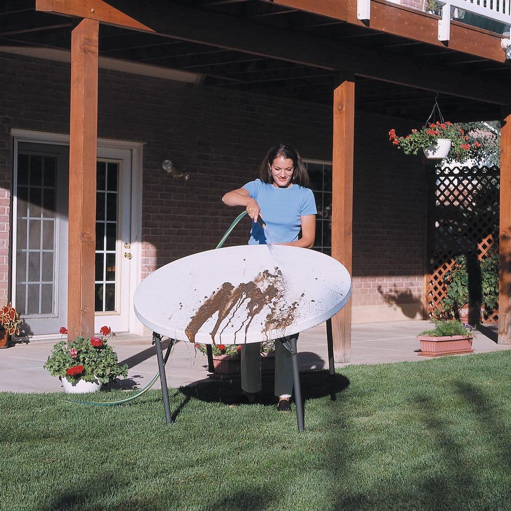 A woman cleaning a white round table with a hose.