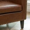 Detail of the nailhead trim and leg of a brown faux leather chair.