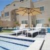 Three white outdoor lounge chairs on a patio by a pool.
