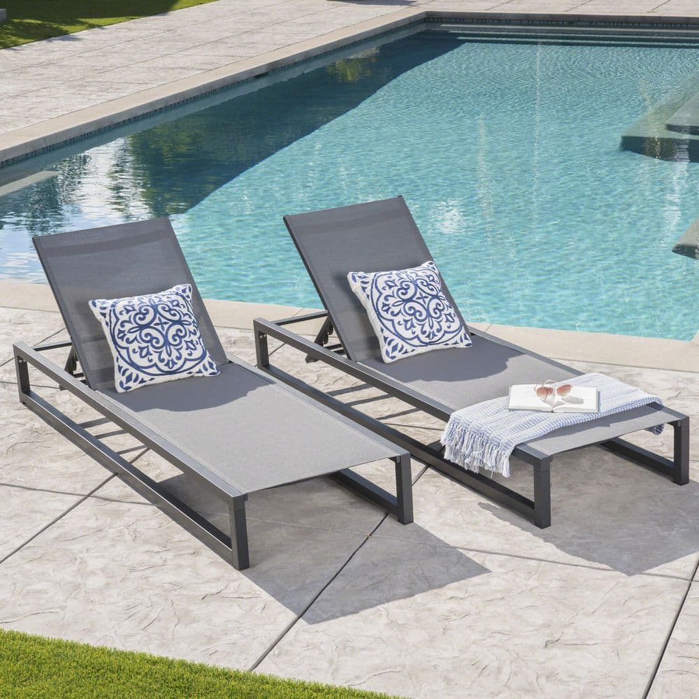 Two grey chaise lounges with patterned pillows by a pool.