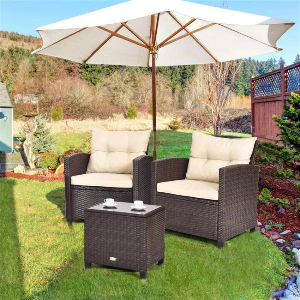 Brown wicker outdoor lounge set with white cushions and a side table placed under a white patio umbrella.