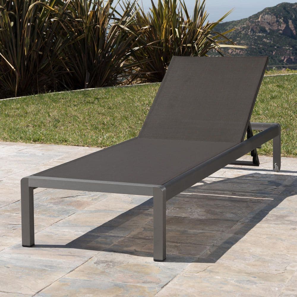 Gray metal outdoor chaise lounge set up outdoors with greenery in the background.