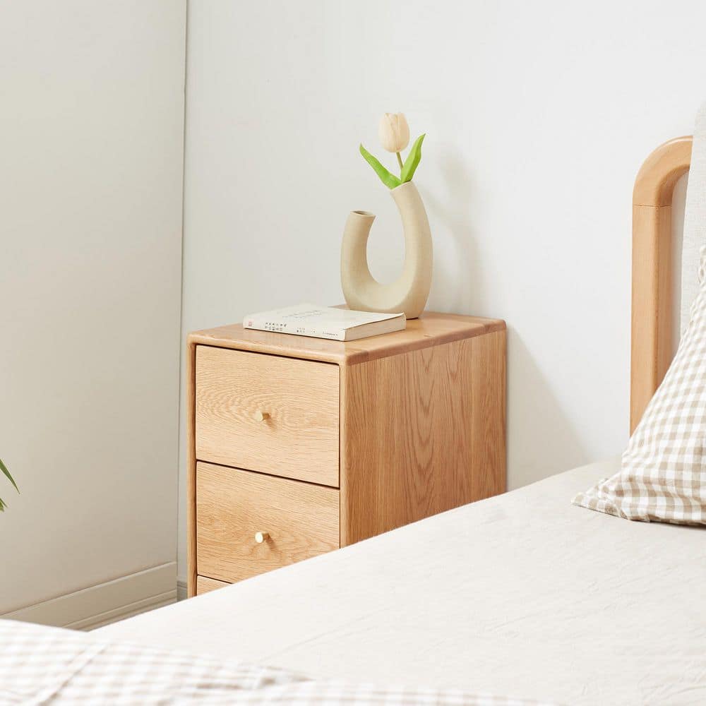 Side angle view of a natural oak accent cabinet with three drawers.