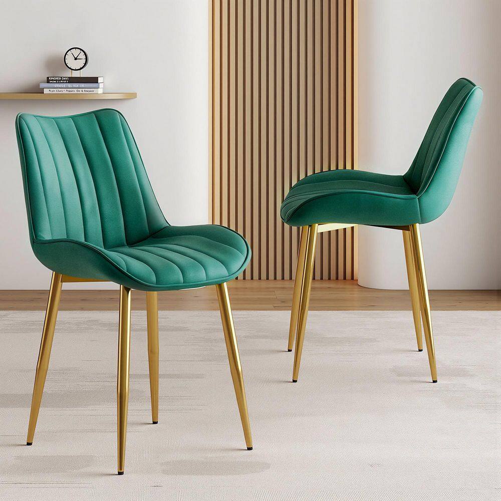 Two green velvet dining chairs with gold legs in a minimalist room.
