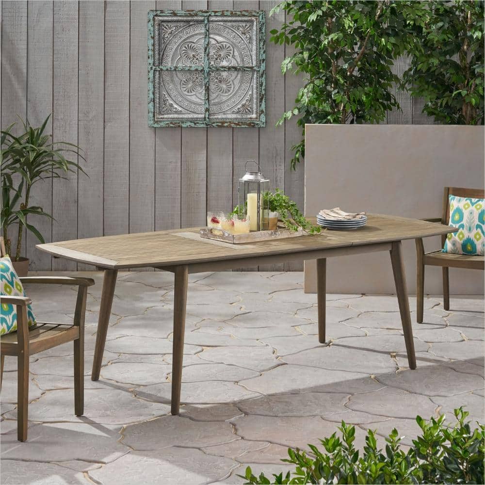 Expandable acacia wood rectangular dining table in neutral gray in an outdoor setting.