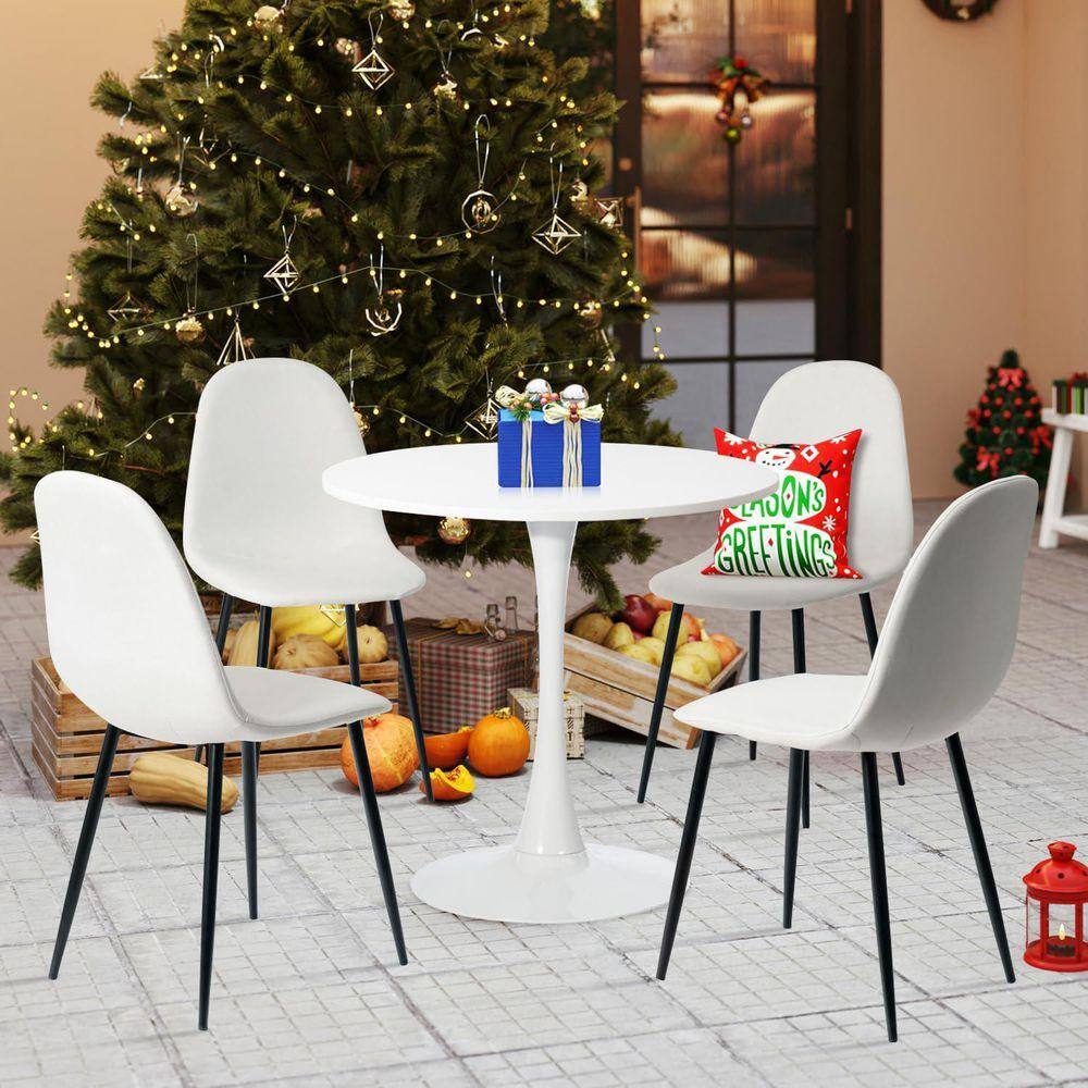 Four beige upholstered dining chairs with black metal legs around a white table near a Christmas tree.