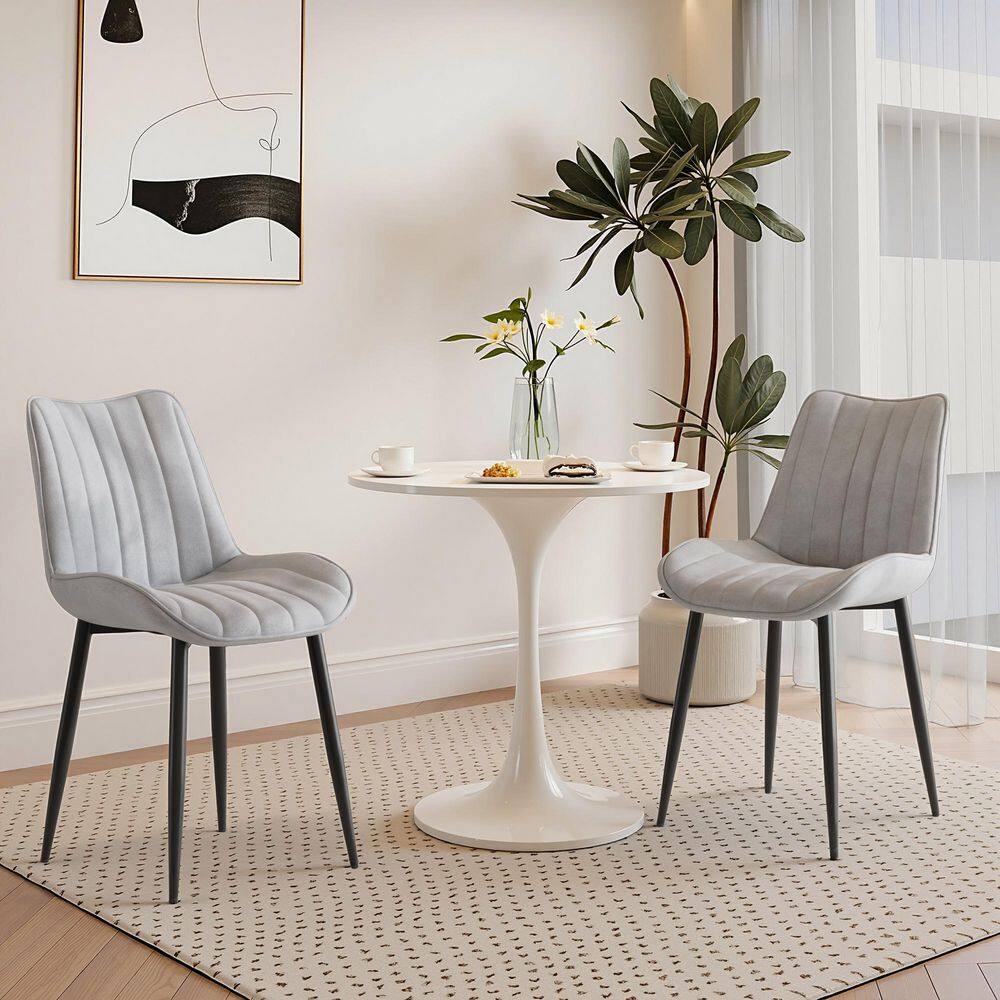 Two gray velvet dining chairs positioned around a white tulip table.