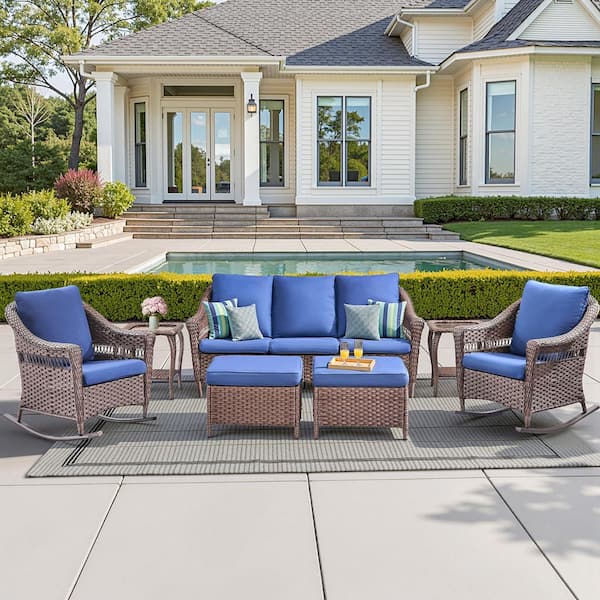 7-piece brown wicker patio furniture set with blue cushions including a sofa, two rocking chairs, two ottomans, and two side tables.