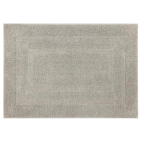 A cream fringe bath rug sits atop gray marble hexagon floor tiles in front  of a roll top freestanding …