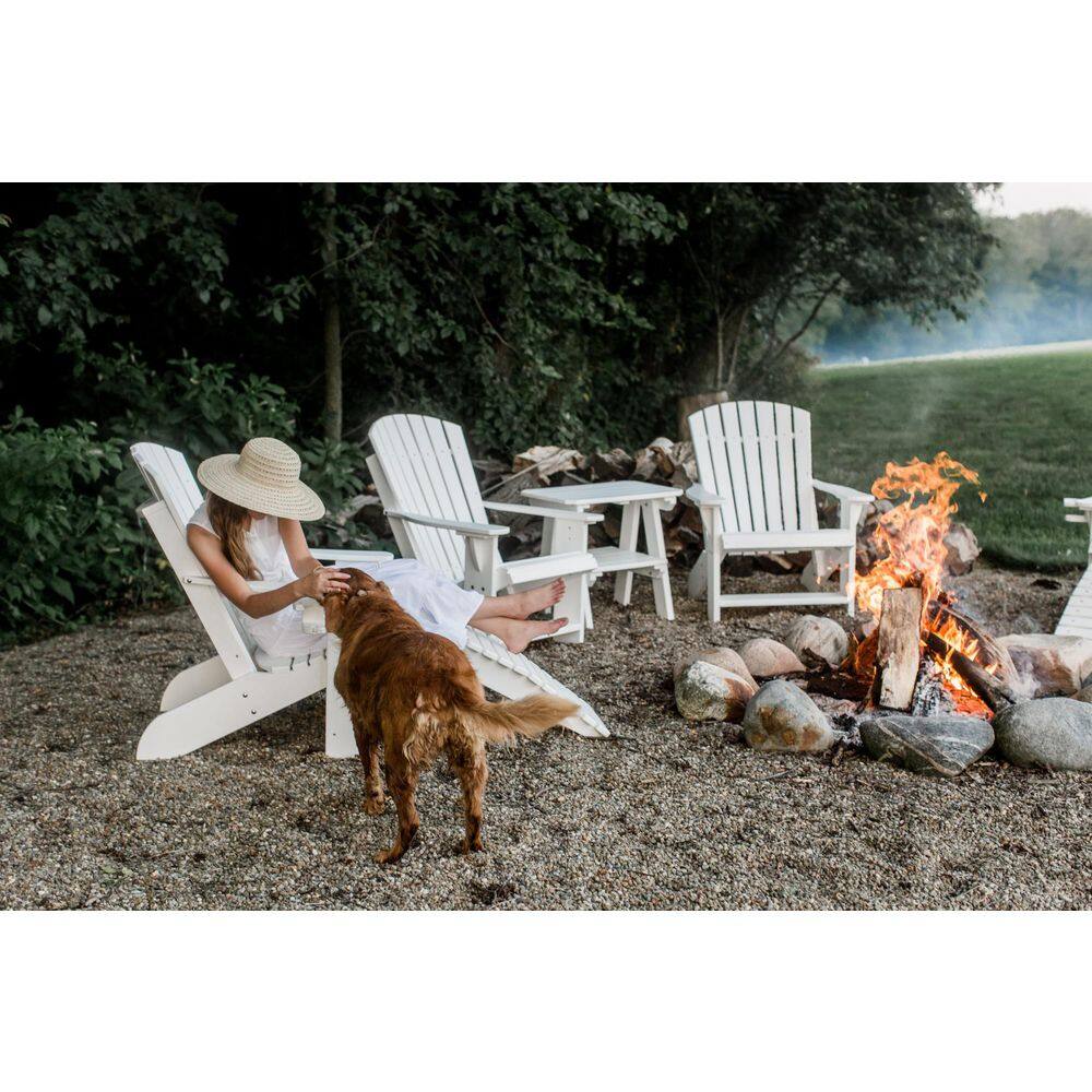 A woman and a dog relaxing in white Adirondack chairs by a fire pit.