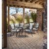 Hanover Lavallette 7-piece patio dining set with a glass table and six grey cushioned chairs under a wooden pergola.