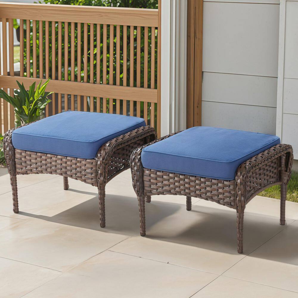 Two brown wicker outdoor ottomans with blue cushions.