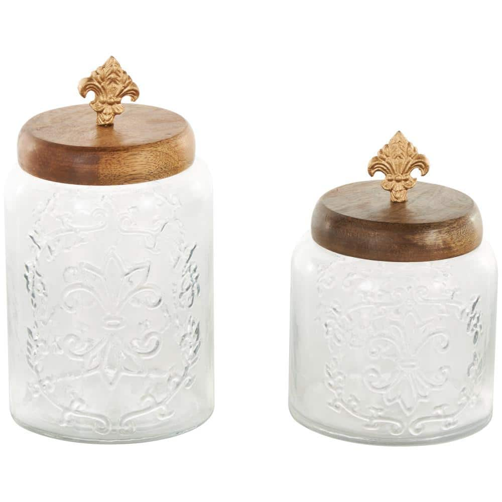 Litton Lane Clear Glass Scroll Decorative Jars with Brown Wooden Lids and Gold Fleur-De- Lis Knobs (Set of 2)