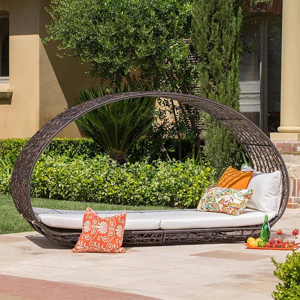 Multi-brown wicker outdoor day bed with colorful accent pillows.