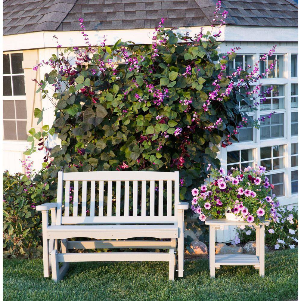 White plastic outdoor glider bench placed on a lawn in front of a house with flowers.