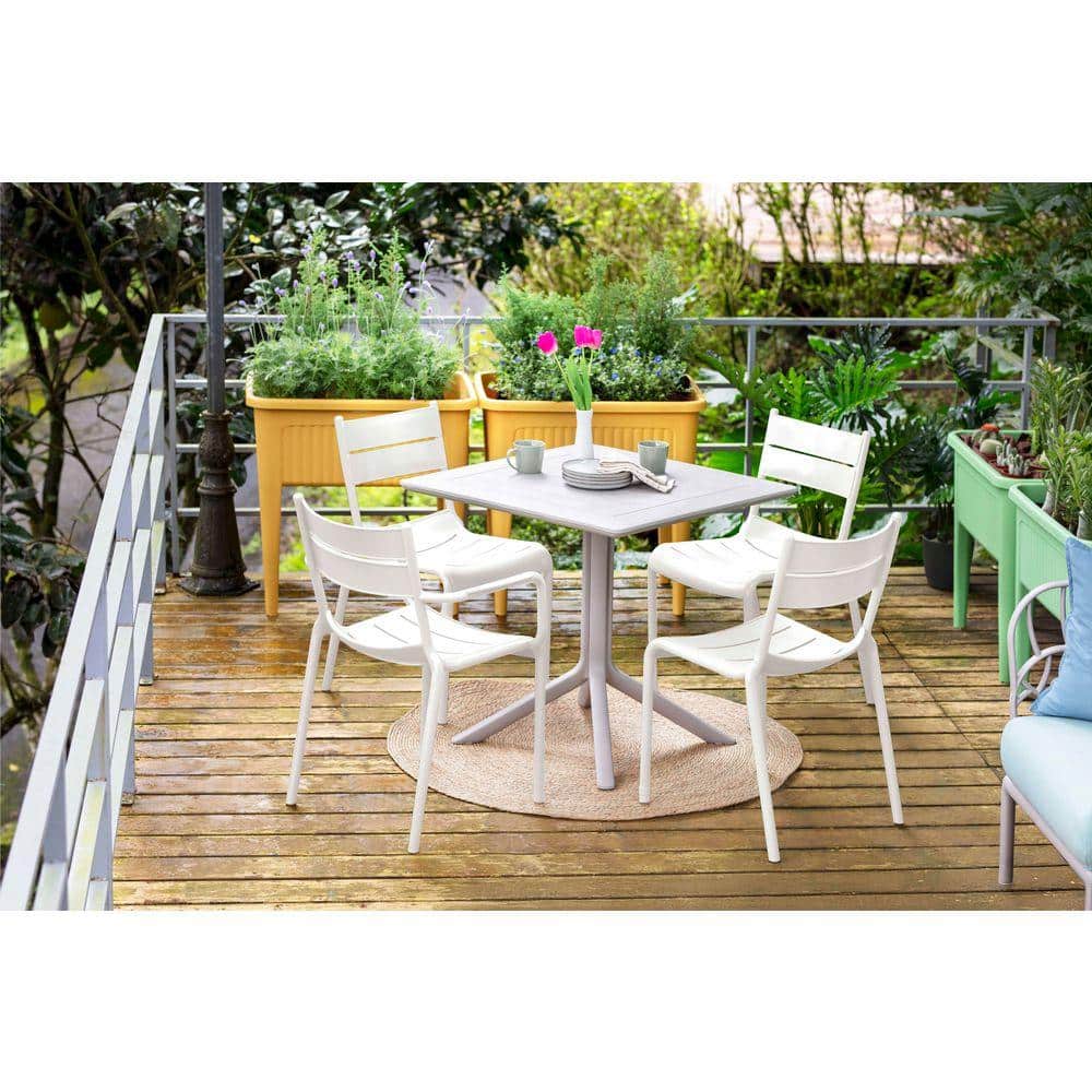 Outdoor dining set with white chairs and plants on a wooden deck.