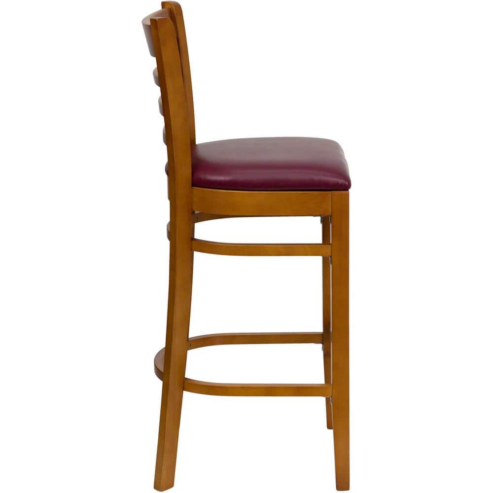 Side view of a burgundy vinyl seat bar stool with a cherry wood frame.