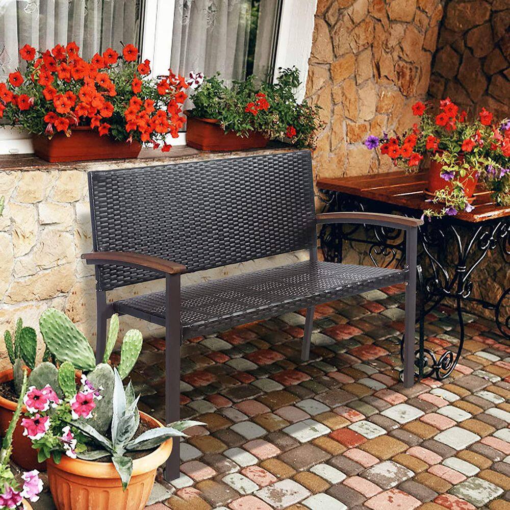 Dark brown rattan bench placed on a stone patio near flowers.