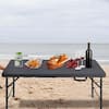 Black folding picnic table set up on a beach with food and wine.