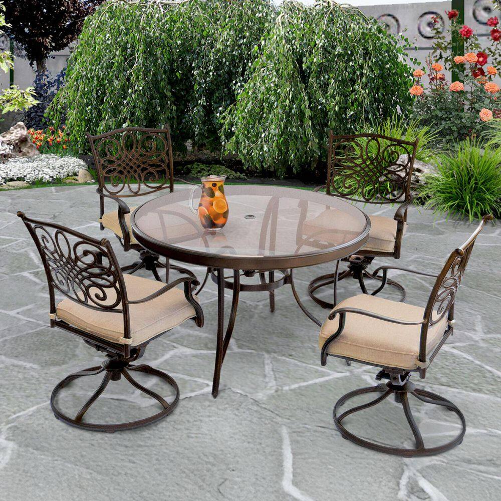 Hanover Traditions 5-piece outdoor dining set with a round glass-top table and four swivel chairs with oat cushions set by a swimming pool.