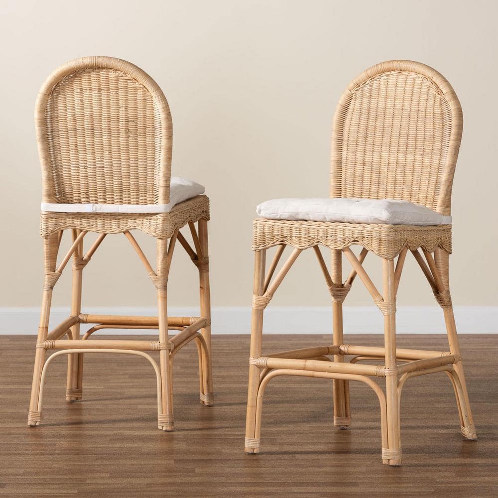 Two natural rattan bar stools with white cushions against a neutral wall.