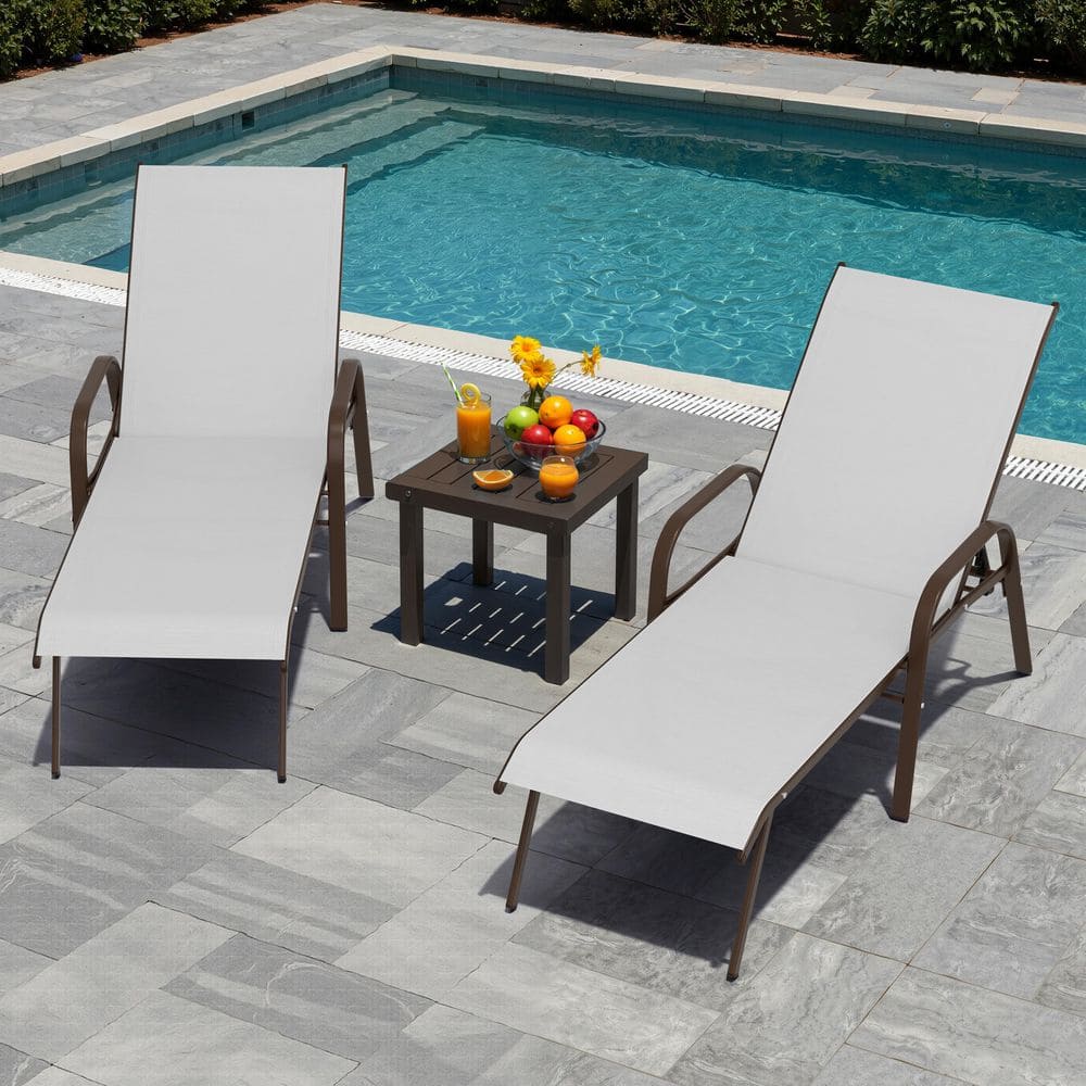 Two light gray chaise lounge chairs positioned around a small brown side table by a pool.