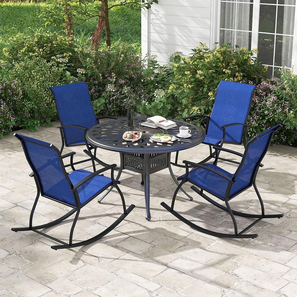 Four navy blue rocking chairs and a round black patio table set in a garden.