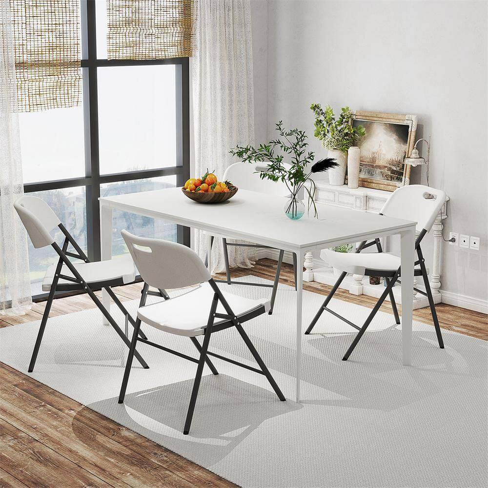 Four white folding chairs arranged around a white dining table in a bright room.