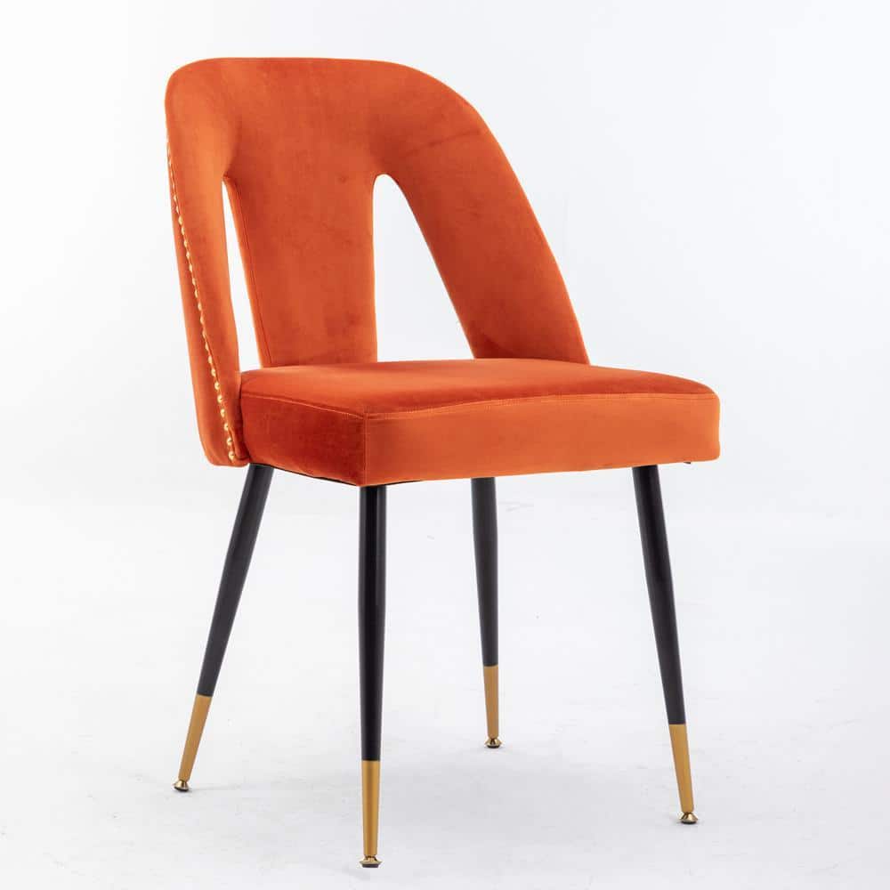 A single orange velvet dining chair with a cutout back and gold nailhead trim.