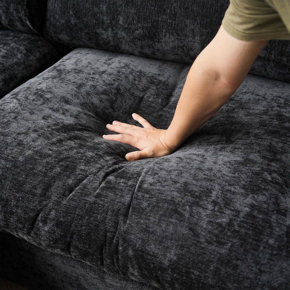 Close-up of a hand pressing into the black chenille fabric of a sofa cushion.