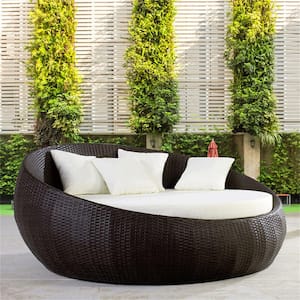 Outdoor black rattan lounge chair with white seat cushion and four white throw pillows.