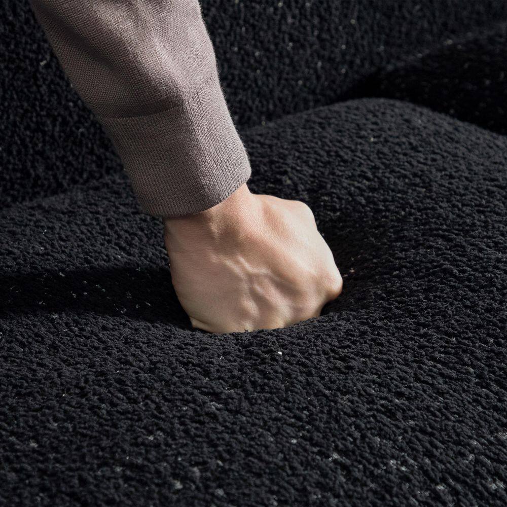 Close-up of a hand pressing into the black boucle fabric of the loveseat.