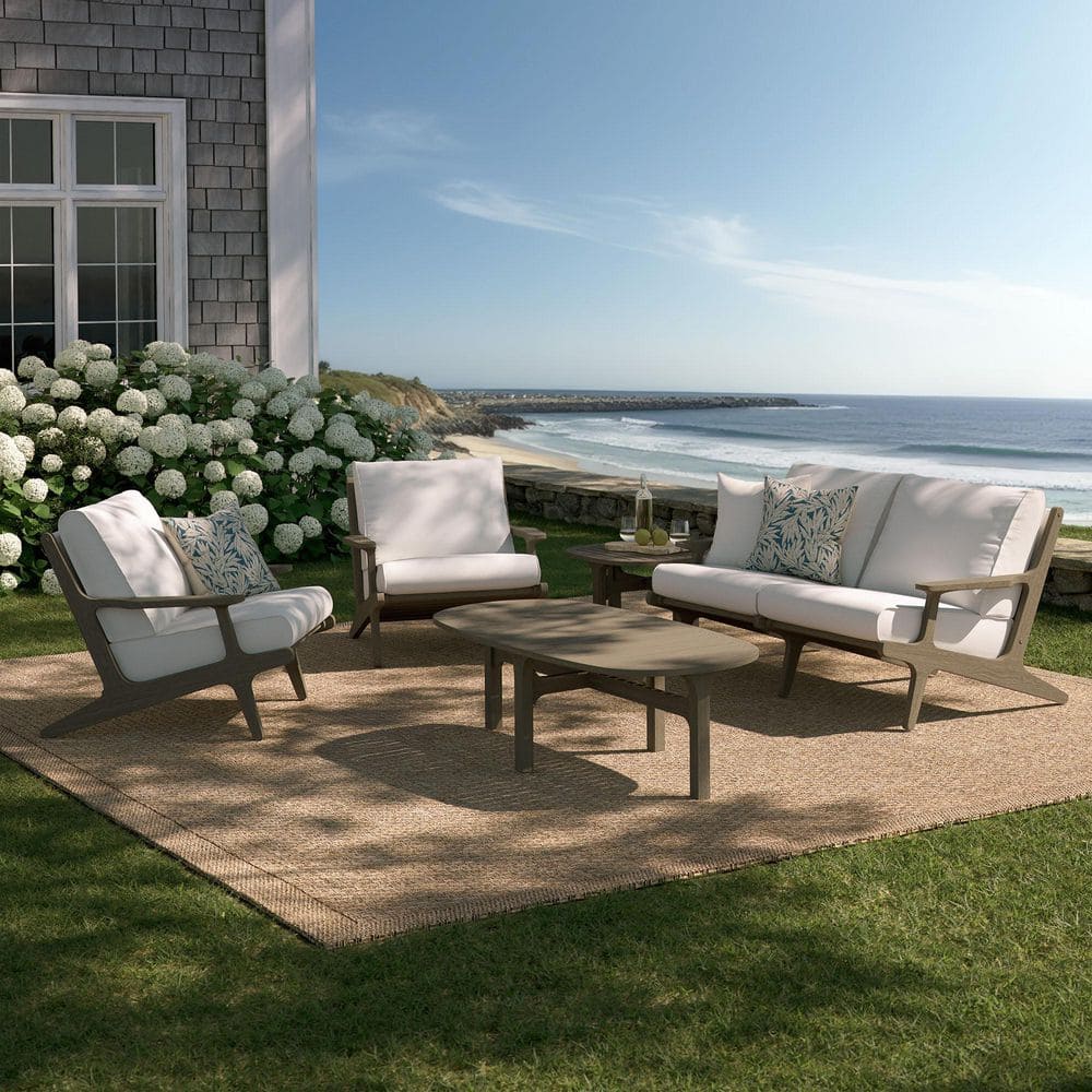 A weathered gray outdoor patio furniture set arranged on a rug by the ocean.