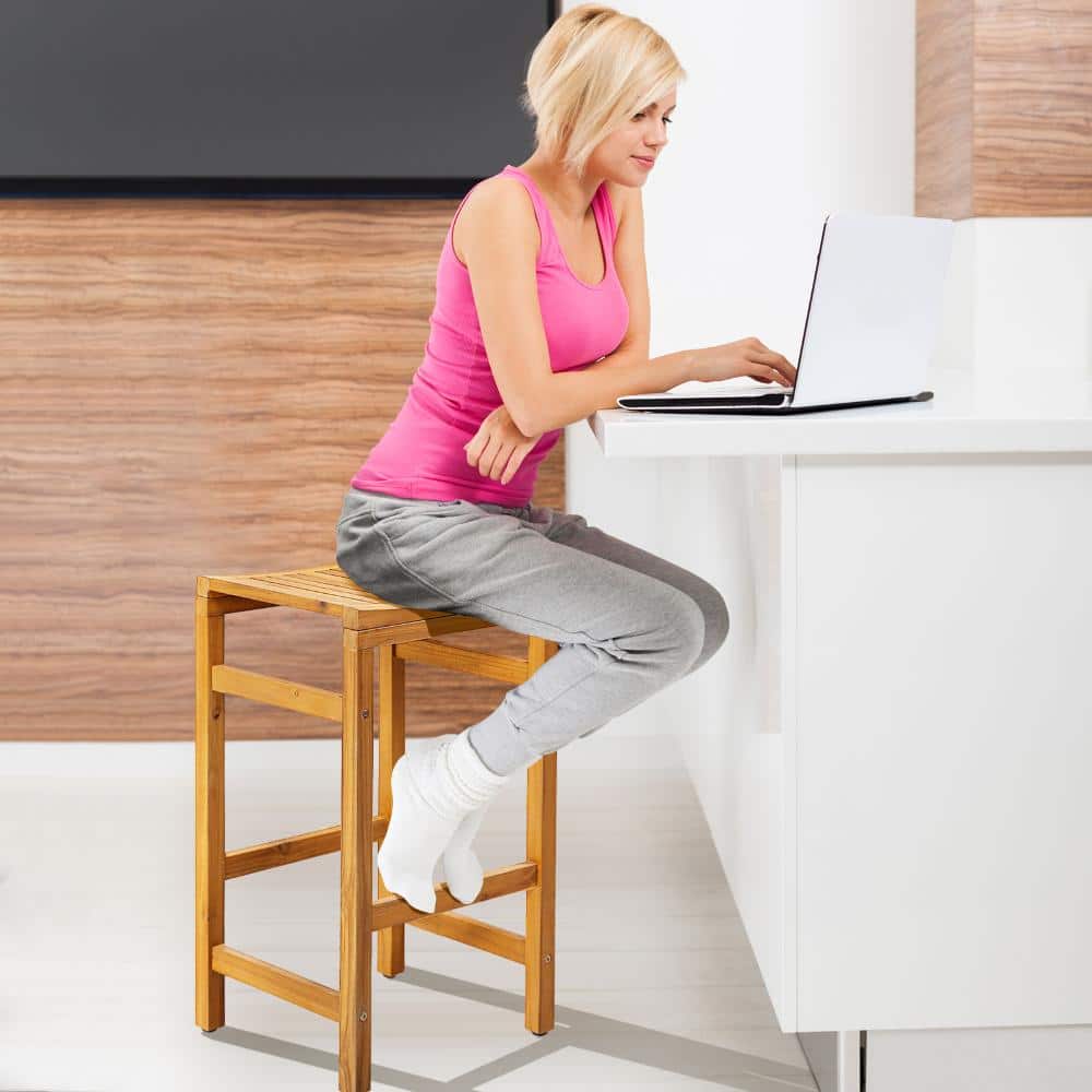 A woman sitting on an acacia wood bar stool using a laptop.