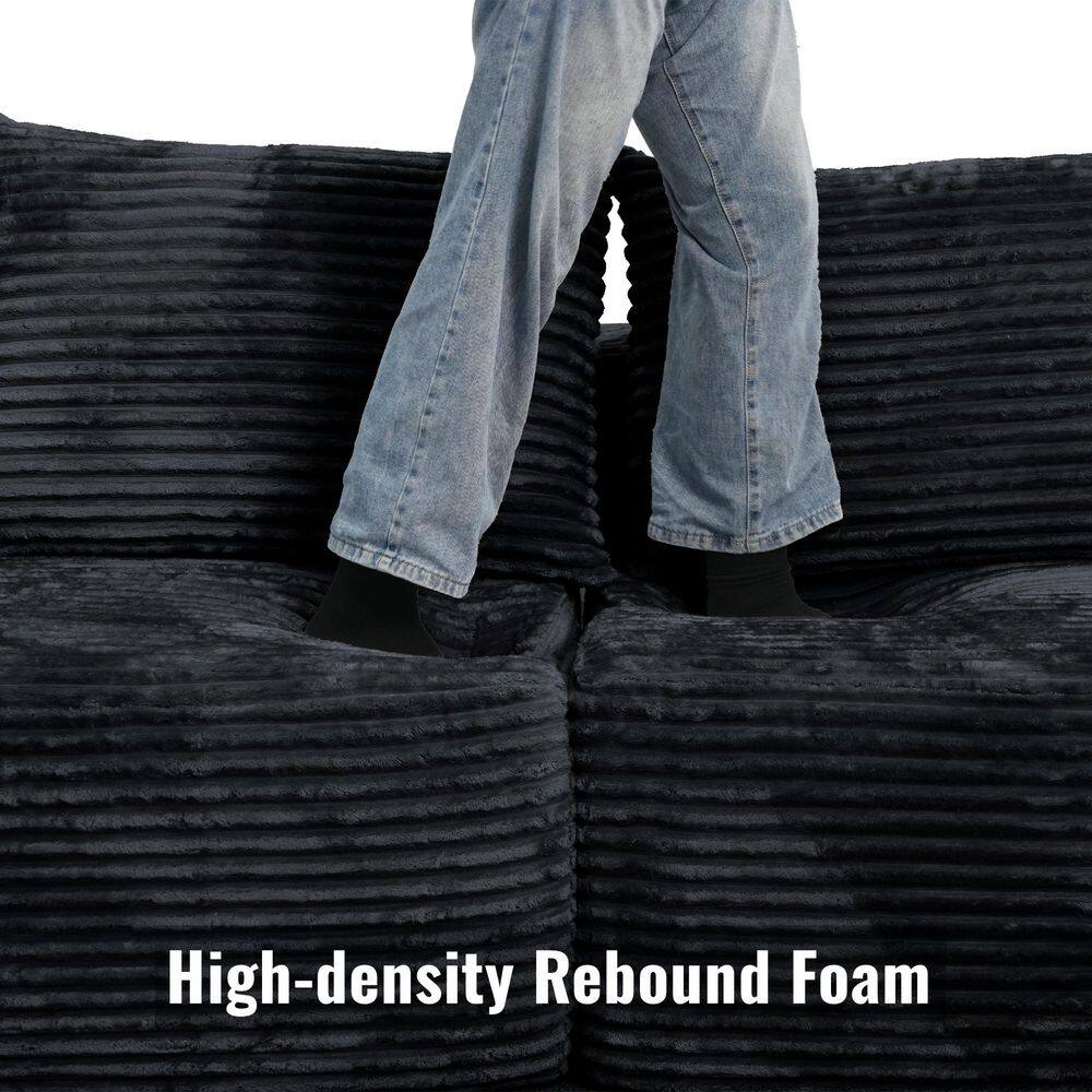 Person stepping on a black corduroy sofa to demonstrate high-density foam.
