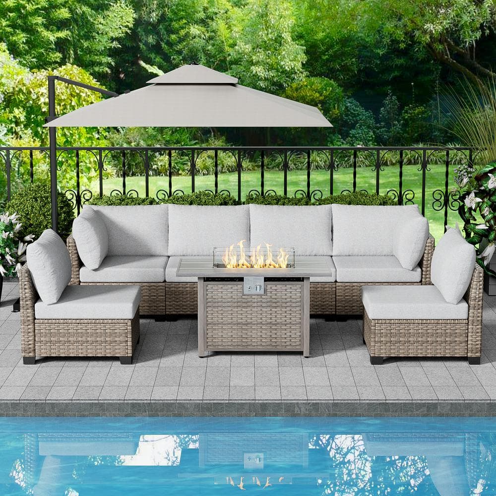 Brown wicker patio conversation set with gray cushions and a fire pit table by a pool.